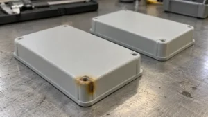 Two matching light gray injection-molded enclosure covers, one with a small brown burn mark near its corner and one without discoloration