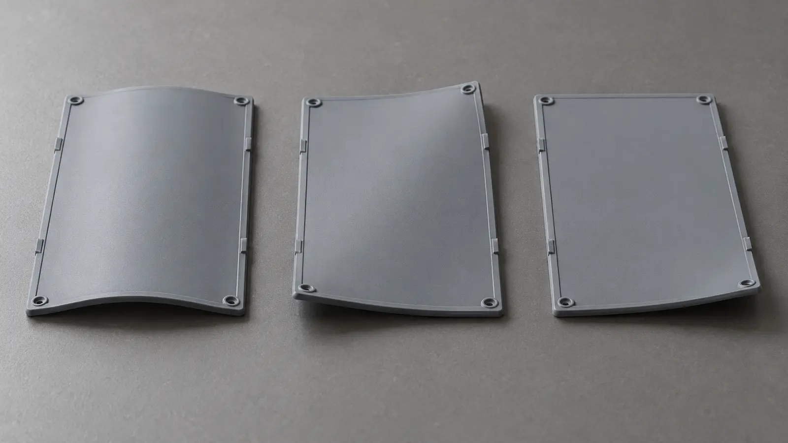 Three matching molded plastic panels showing bowing, twisting, and a lifted corner on a flat reference surface