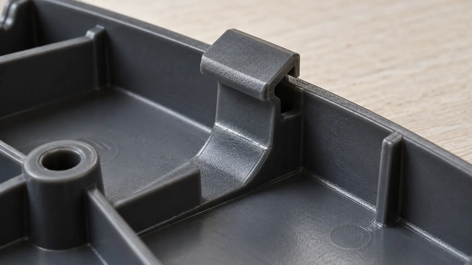Underside of an injection-molded cover showing a flexible snap-fit tab and a fine knit line at the tab root.